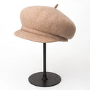 Beige beret on a black stand against a white background, Obroi