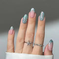 Hand with glittery nails wearing two rings on a neutral background, Obroi