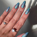 Hand with blue glittery nails and rings on a neutral background, Obroi