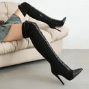 Black over-the-knee boots with lace-up design worn by a person sitting on a beige couch, Obroi