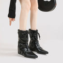 Black leather boots with pointed toes and lace-up design worn by a person on a light gray background, Obroi