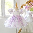 White dress with purple floral patterns on a mannequin in a bright room, Obroi