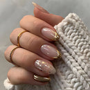 Obroi Hand with gold and nude nail polish holding a white knitted fabric.
