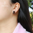 Close-up of a person wearing a square earring with a blurred natural background, Obroi