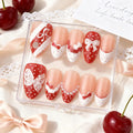 Set of decorative false nails with red and white designs in a clear box, surrounded by cherries and lace, Obroi