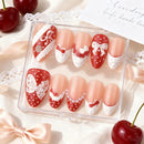 Set of decorative false nails with red and white designs in a clear box, surrounded by cherries and lace, Obroi