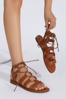 Brown strappy sandals being held by a hand on a white background, Obroi