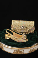 A gold embellished slingback sandal with a matching chain bag, both decorated with rhinestones and a bow, displayed on a dark green velvet surface against a black background, Obroi