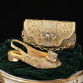 A gold embellished slingback sandal with a matching chain bag, both decorated with rhinestones and a bow, displayed on a dark green velvet surface against a black background, Obroi
