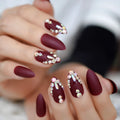 Maroon nails with rhinestone embellishments on a blurred background ,Obroi