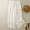 White lace-trimmed pants with a woven bag and white shoes on a beige background, Obroi