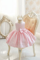 Pink dress with a large bow and lace details on a mannequin against an ornate chair and mirror, Obroi