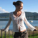 Woman in a white lace top standing by a lake with mountains in the background