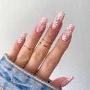Hand with pink floral nail design wearing gold rings on a light gray background, Obroi