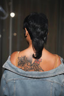 Short black hair styled in a low ponytail, shown from the back on a person with a floral tattoo on their upper back, wearing a denim jacket, Obroi