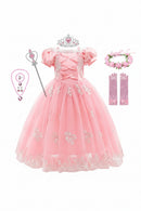 A pink princess costume set for girls, featuring a tulle ball gown with lace appliques, a silver tiara, a wand, a heart-themed necklace, pink satin opera gloves, and a pink floral headband, all arranged on a white background, Obroi