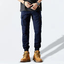 Person wearing navy cargo pants and brown boots on a light gray background, Obroi