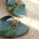 Pair of light blue sandals with green straps and woven details on a textured surface, Obroi