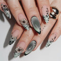 A close-up of a hand with long, embellished almond-shaped nails. The nails feature a mix of pale pink, glossy black and white zebra-like patterns, cat-eye gradient tips, and silver rhinestone floral accents, Obroi