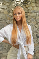 A long straight blonde wig with a center part, shown on a model against a stone wall and also as close-up views of the hair and the black lace underside, Obroi