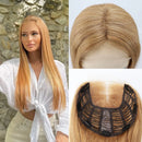 A long straight blonde wig with a center part, shown on a model against a stone wall and also as close-up views of the hair and the black lace underside, Obroi