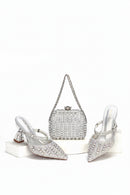 Silver high-heeled shoes, clutch bag, and ring with gemstones on a white background, Obroi