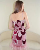 Woman wearing a pink and red floral dress with feather details, sitting on a beige couch, Obroi