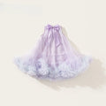 A sleeveless lavender tulle dress for toddlers, featuring a tiered ruffled skirt with pom-pom details and a matching satin bow at the back of the neckline, displayed on a warm cream background, Obroi