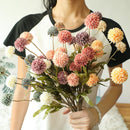 Person holding a bouquet of colorful artificial flowers against a neutral background, Obroi