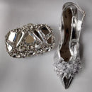 Silver high-heeled shoe with crystal embellishments and matching clutch on a gray background, Obroi