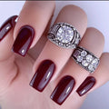 Hand with burgundy nails wearing two silver rings with gemstones on a white background, Obroi
