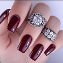 Hand with burgundy nails wearing two silver rings with gemstones on a white background, Obroi