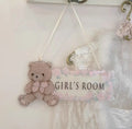 A hanging decorative sign for a girl's room featuring a teddy bear on the left and the words 'GIRL'S ROOM' on the right, with a pink floral border and white ribbon cords for hanging, Obroi