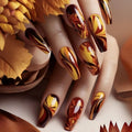 Nails with autumn-themed nail art featuring gold, brown, and red colors, surrounded by fall leaves, Obroi