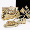 A coordinated gold women's accessory set on a white and black studio background, including a metallic gold clutch bag with a jeweled clasp, a pair of gold slingback block-heel sandals with jeweled toe embellishments, and a matching gold handbag displayed on clear stands, Obroi