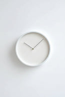A minimalist round wall clock with a matte white frame and a white dial face, featuring slim black hands and a small gold center accent. The brand name 'Obroi' is printed in small gold letters near the top.