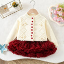 A toddler girl's two-piece knit outfit set, featuring a cream-colored cardigan sweater with red buttons and a matching deep red ruffled tutu skirt, displayed on a wooden hanger against a textured white background, Obroi