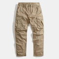 A pair of khaki cargo pants laid flat against a light gray background, featuring multiple utility pockets and a button closure, Obroi