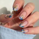 Nails with floral design held by a hand against a neutral background, Obroi