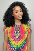 Woman with curly hair wearing a colorful tie-dye shirt against a plain background, Obroi