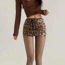 A model wearing a brown ribbed long-sleeve crop top and a leopard-print mini skirt covered in sequins, paired with sheer black tights, against a plain light gray background, Obroi
