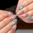 A close-up of a hand with manicured nails featuring a pastel pink and light blue floral design with gold foil accents, Obroi