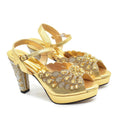 Gold high-heeled shoes with floral embellishments on a white background, Obroi