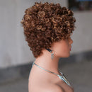 A side-profile view of a mannequin wearing a short, tightly curled brown wig with warm golden highlights, styled with silver hoop earrings and a silver necklace against a soft gray background, Obroi