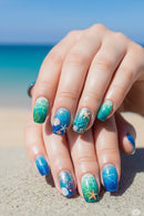 Nails with ocean-themed design held on a sandy background, Obroi