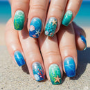 Nails with ocean-themed design held on a sandy background, Obroi