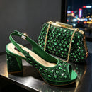 A pair of green embellished slingback high-heeled shoes displayed with a matching green rhinestone clutch bag on a reflective dark surface, with a blurred city lights background, Obroi
