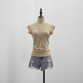 A beige short-sleeve top with small black polka dots and a split neckline, displayed on a mannequin torso with light-wash denim shorts against a plain light gray background, Obroi
