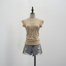 A beige short-sleeve top with small black polka dots and a split neckline, displayed on a mannequin torso with light-wash denim shorts against a plain light gray background, Obroi