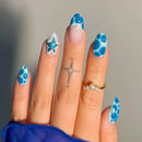Hand with blue and white patterned nails against a neutral background, Obroi